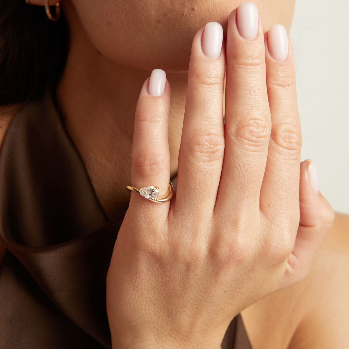 Model. A close-up lifestyle shot of a woman wearing a gold ring with a floating pear diamond. 