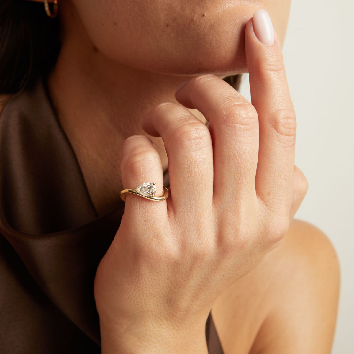 A close-up lifestyle shot of a woman wearing a gold ring with a floating pear diamond. 