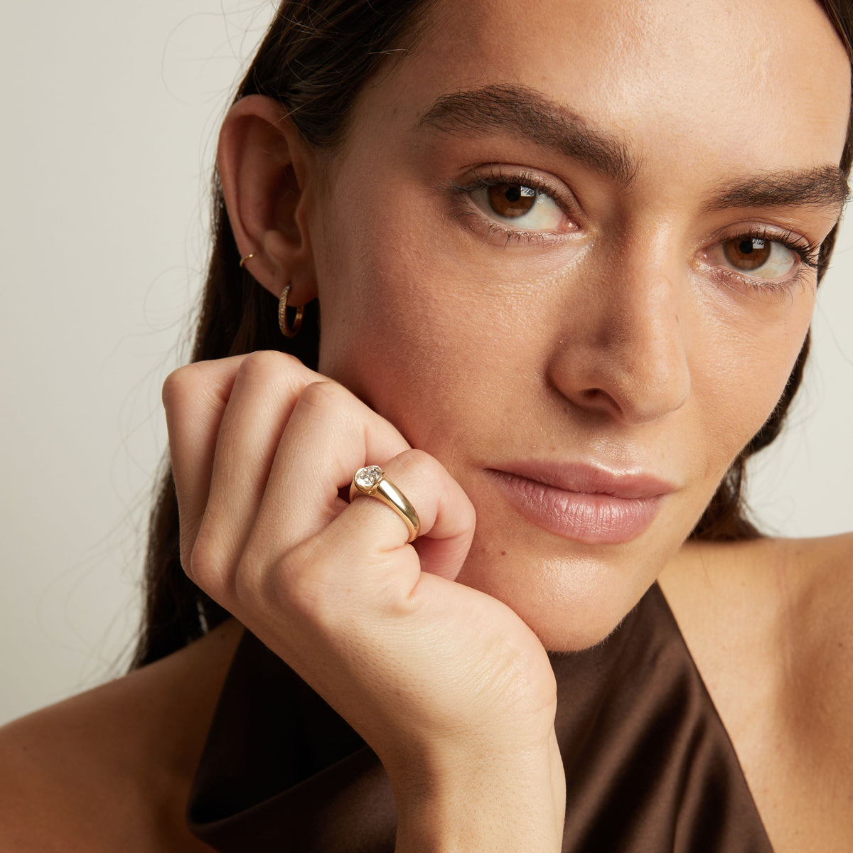 Model. A close-up lifestyle shot of a woman wearing a gold signet ring with a round diamond. 