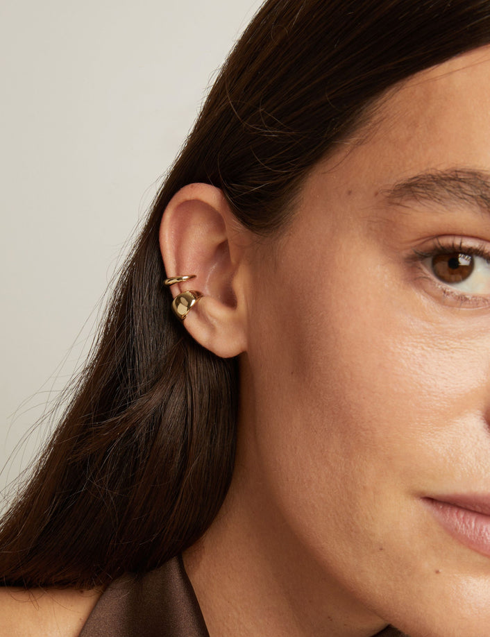 Model. Close up of woman wearing two gold ear cuffs. 