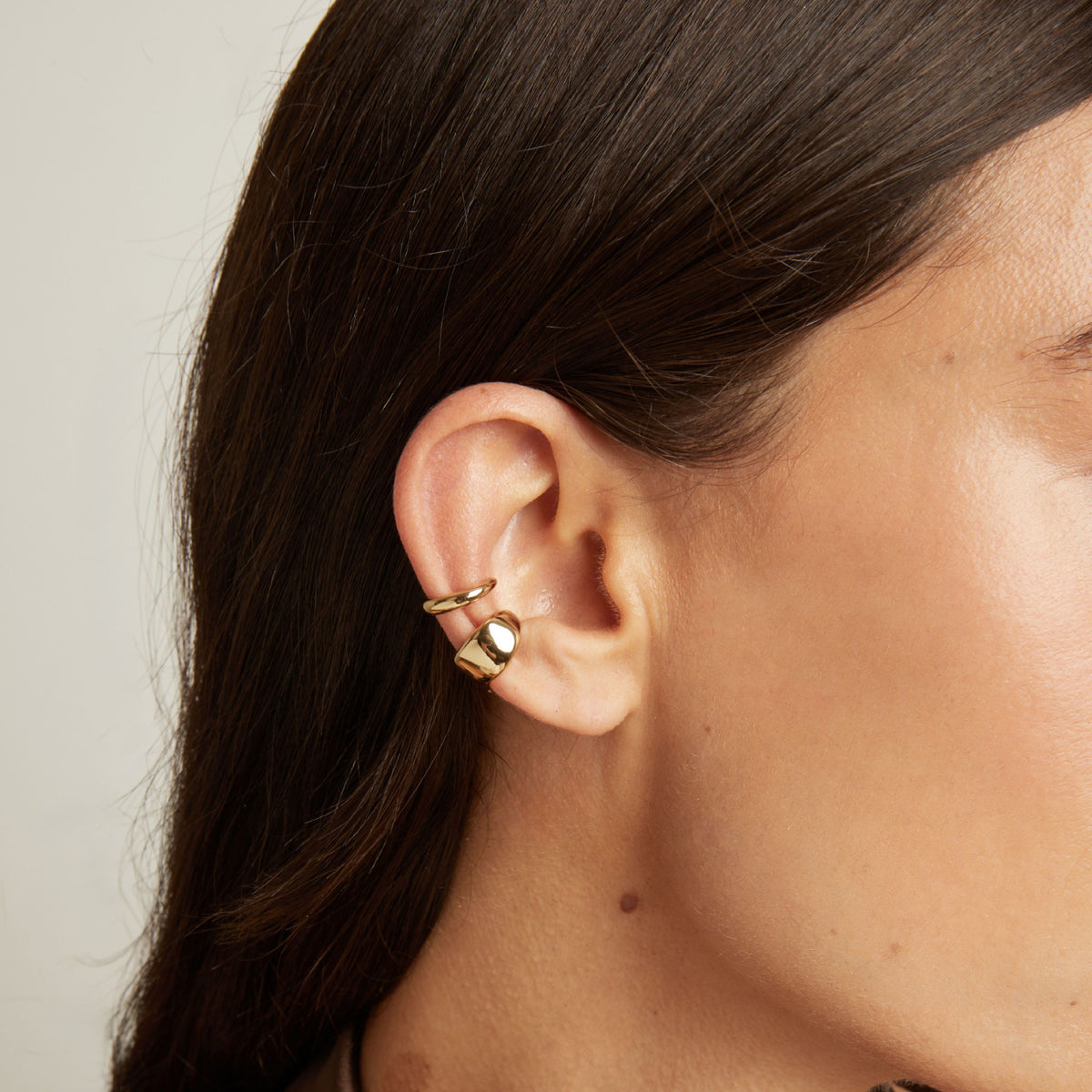 Model. Close up of woman wearing two gold ear cuffs. 