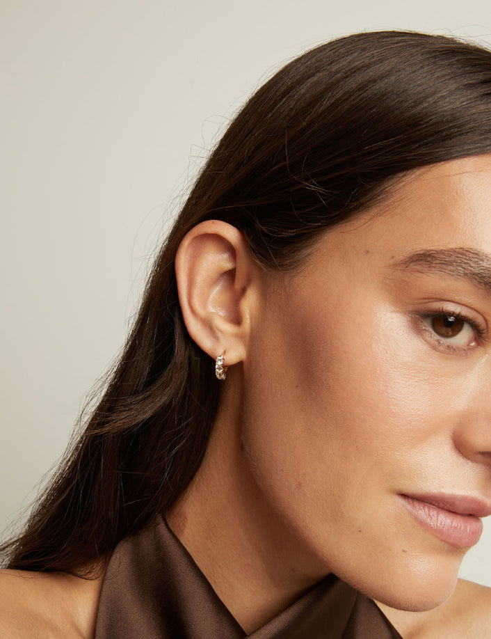 Close up of woman wearing a white sapphire huggie earring on a neutral background.