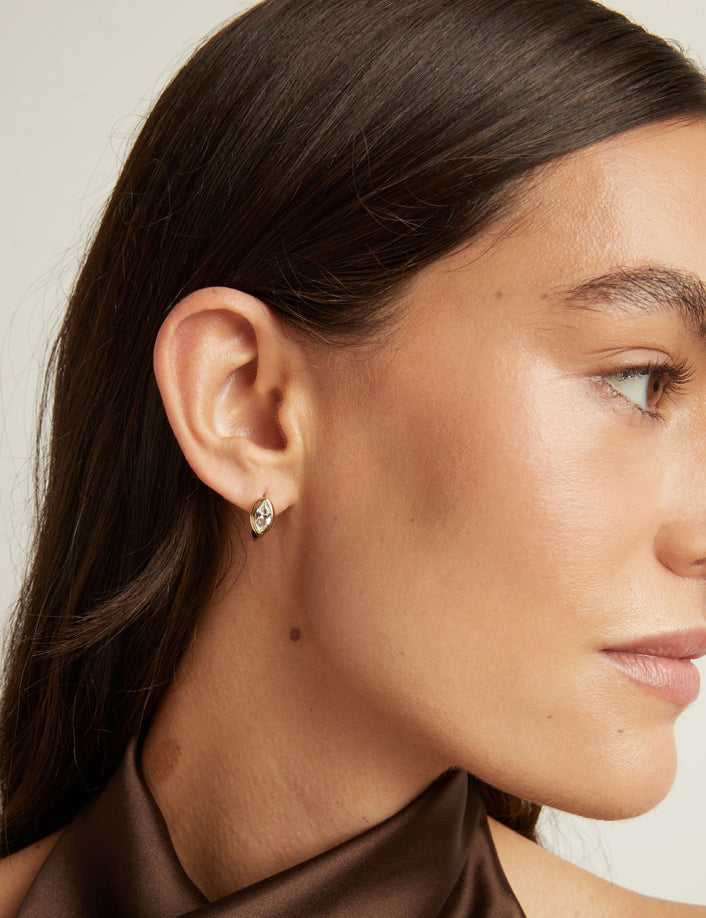 Model. Close up of woman wearing a gold bezel huggie earring on neutral background.