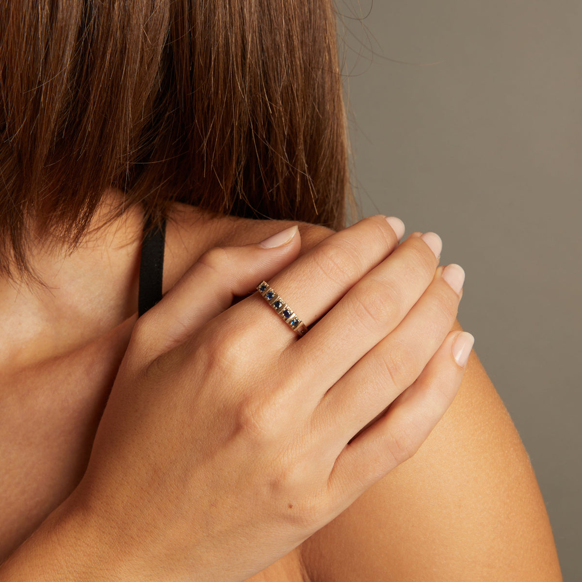 Model. Close up of woman wearing a blue sapphire gold ring on neutral background.