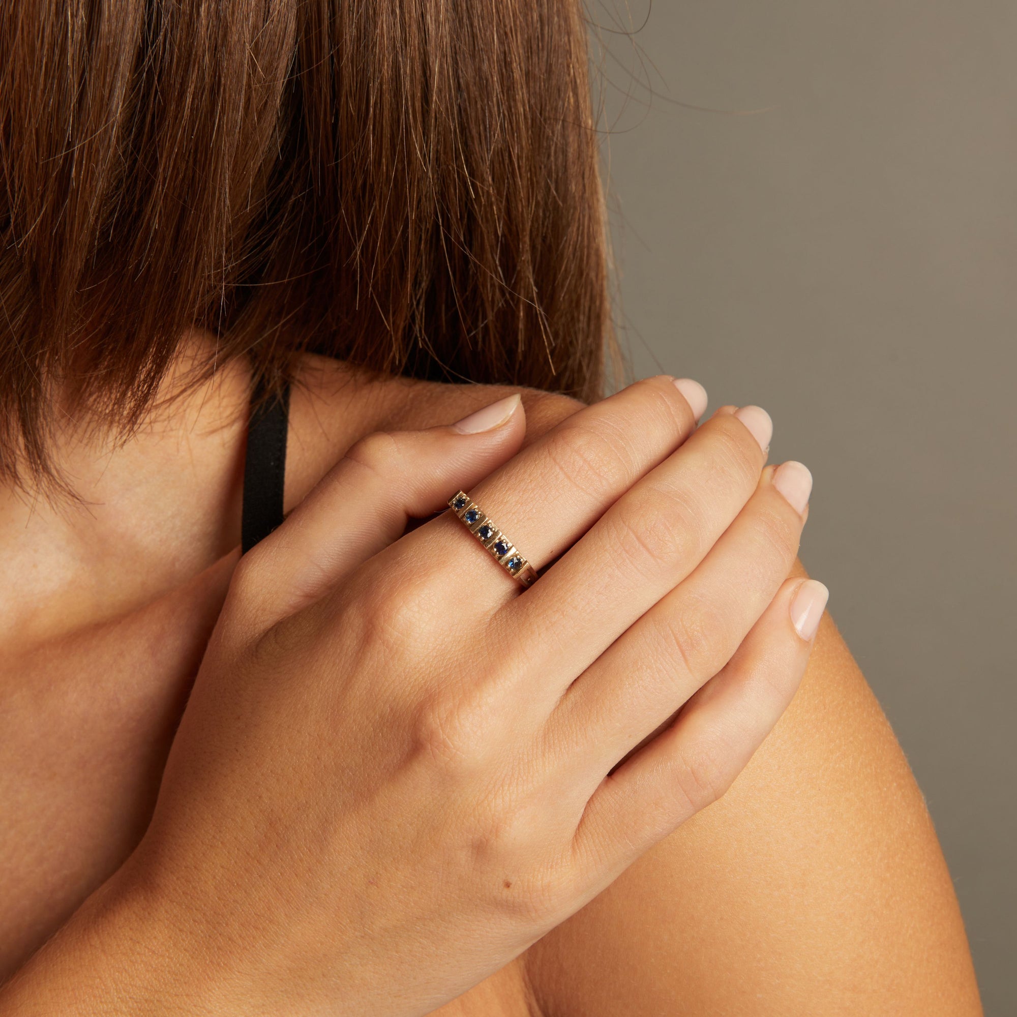 Model. Close up of woman wearing a blue sapphire gold ring on neutral background.