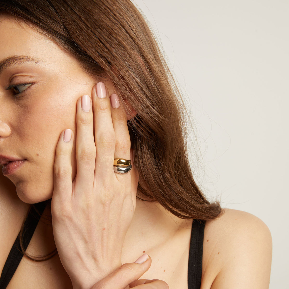 Woman with long brown hair wearing rings and touching her face.