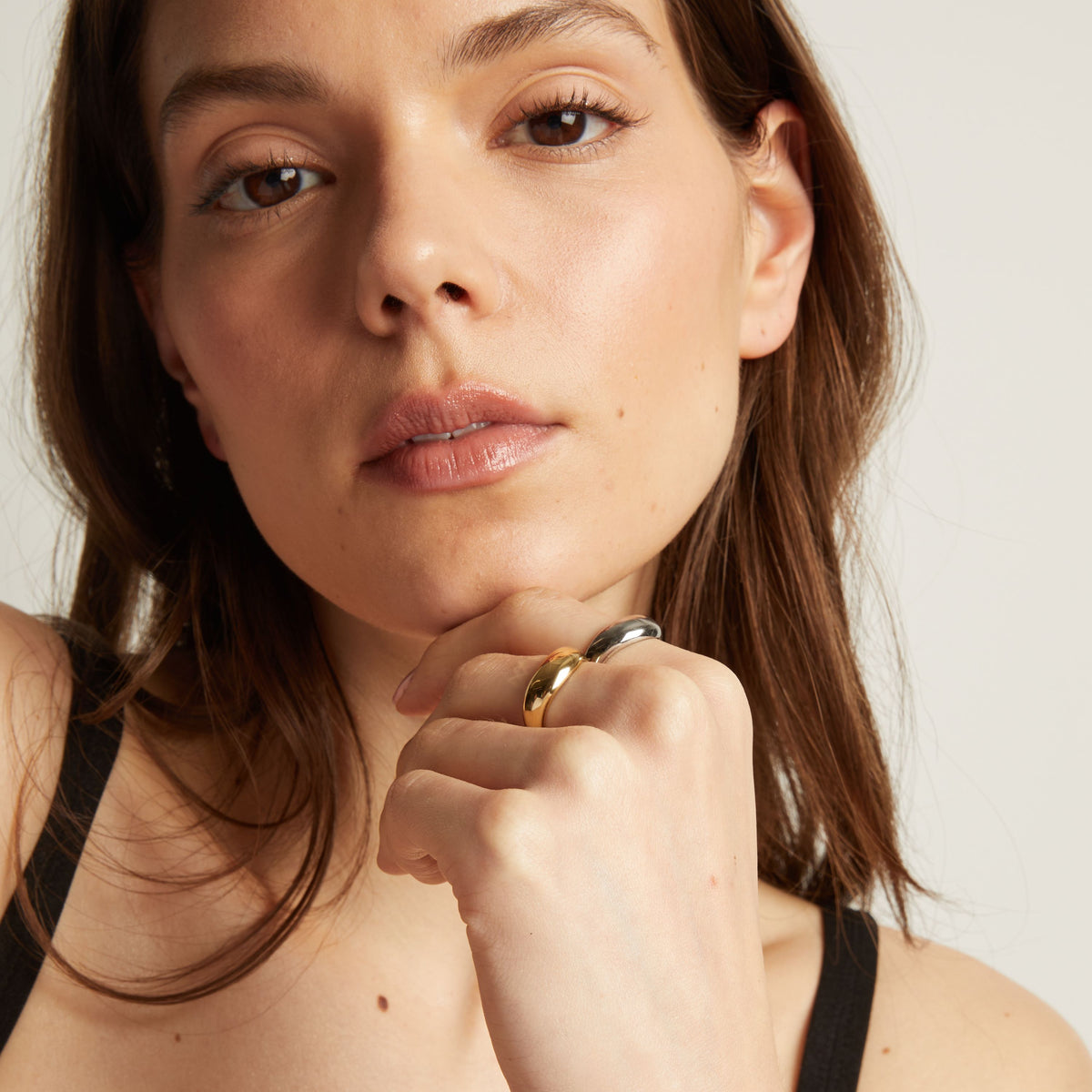 Model. Close up of a woman with gold and silver rings on her finger, touching her face.