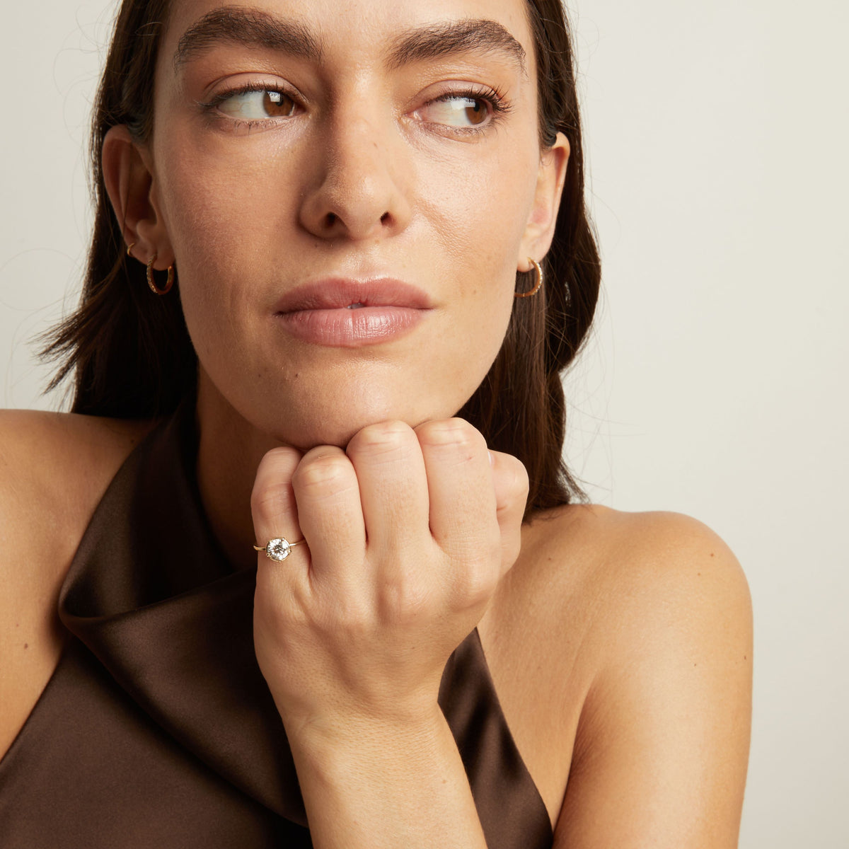 Model. A close-up lifestyle shot of a woman wearing a delicate gold ring with a round diamond. 