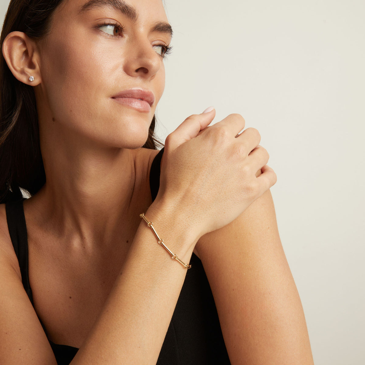 A woman wearing a delicate gold chain bracelet on her wrist, shown in a close-up profile against a plain light background.