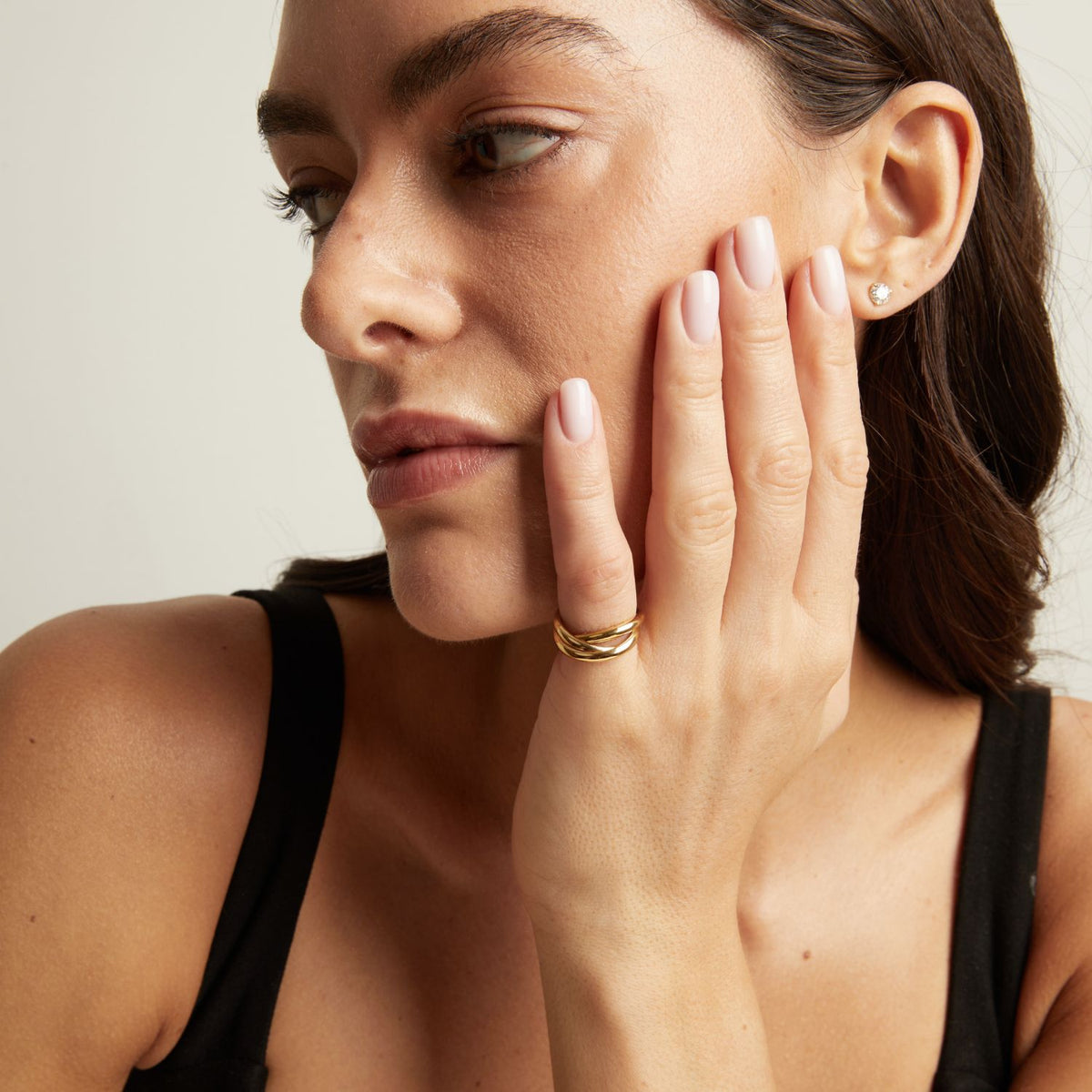 Model. A close-up of a woman's hand wearing a delicate gold ring with three intertwined bands.