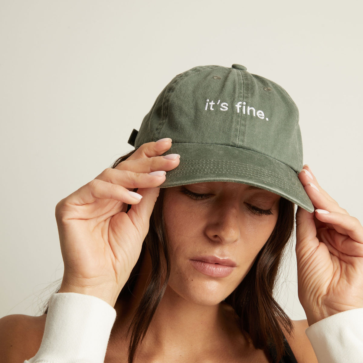 Woman wearing a green cap with 'it's fine' text on a plain background