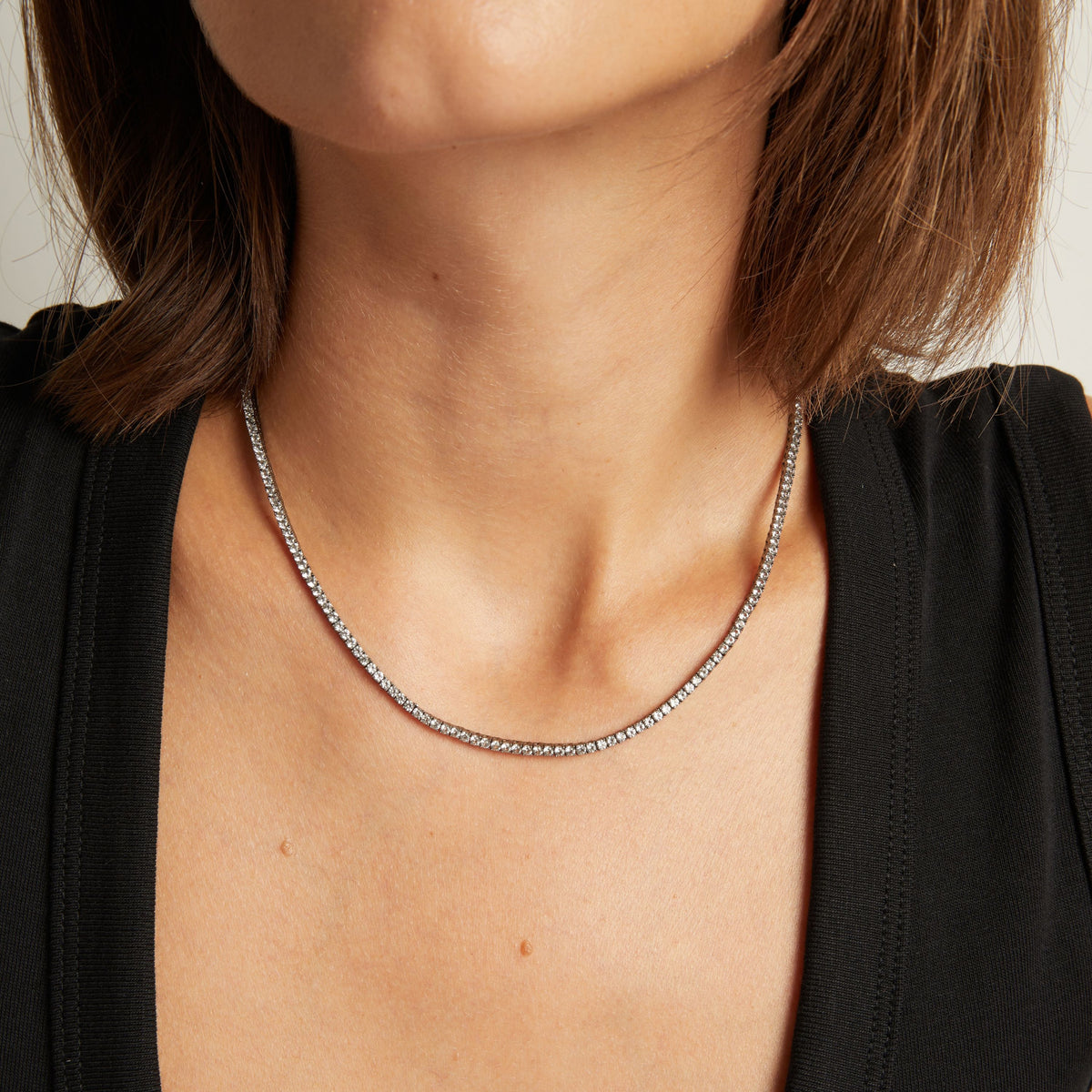 Model. Close up of woman wearing a Black Rhodium Tennis Necklace on neutral background.
