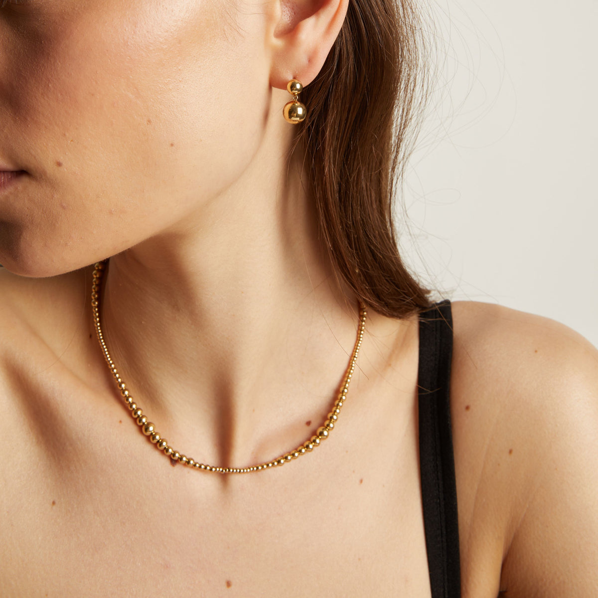 Gold necklace and earrings worn by a person with a neutral background.
