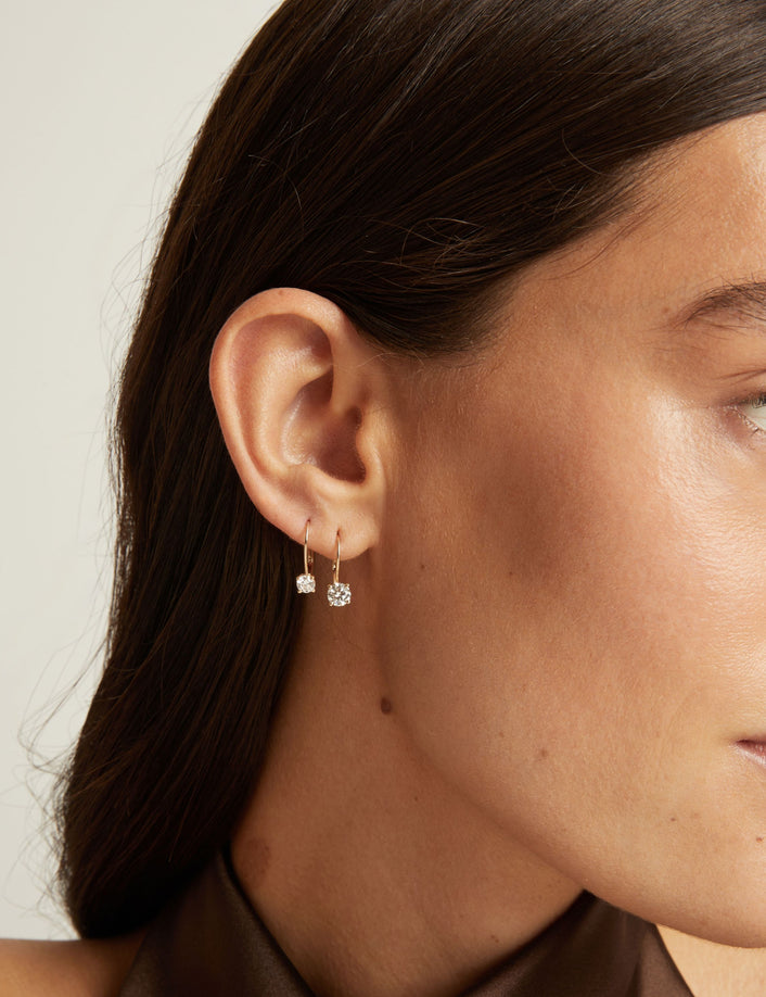 Close up of a woman wearing 2 gold hoop earrings with diamonds on neutral background.
