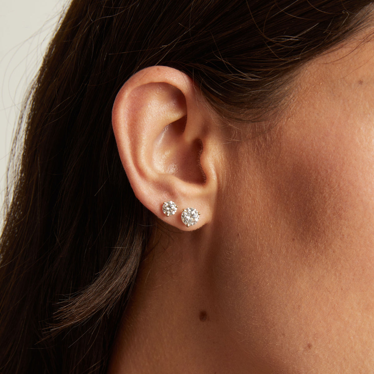 Model. Close up of a woman's ear wearing two diamond stud earrings. 