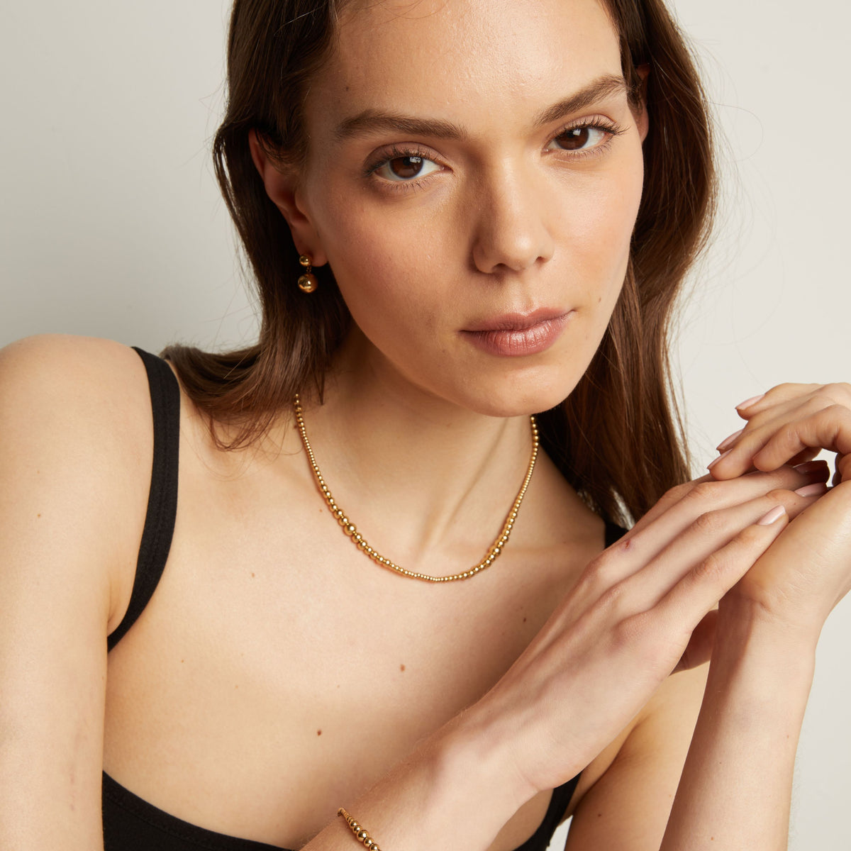 Woman wearing a gold necklace and bracelet with a neutral background.