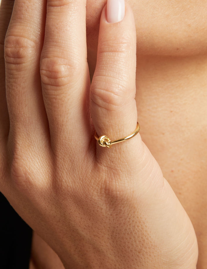 Model. A close-up lifestyle shot of a woman wearing a delicate gold ring with a knotted design on her finger.