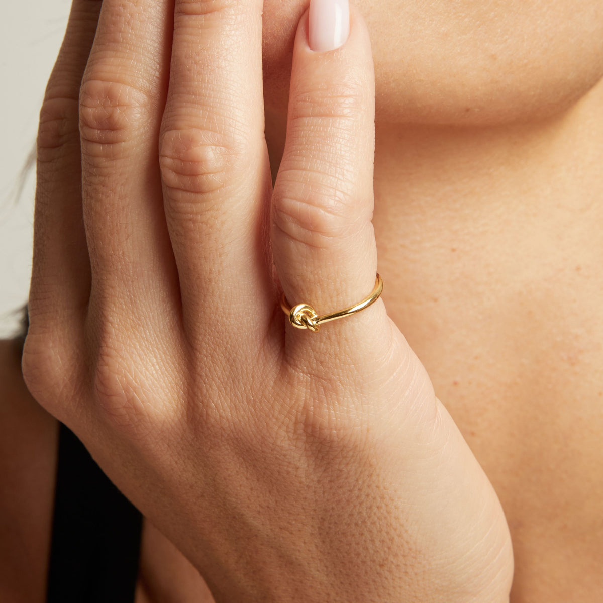 Model. A close-up lifestyle shot of a woman wearing a delicate gold ring with a knotted design on her finger.