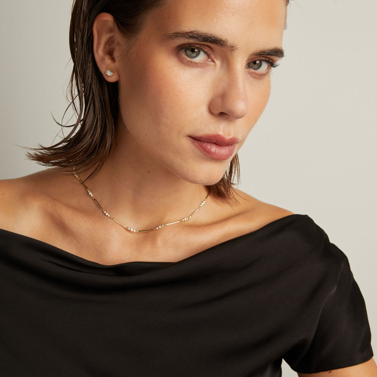 Model. Close up of a woman in a black top wearing a diamond bar necklace on beige background.