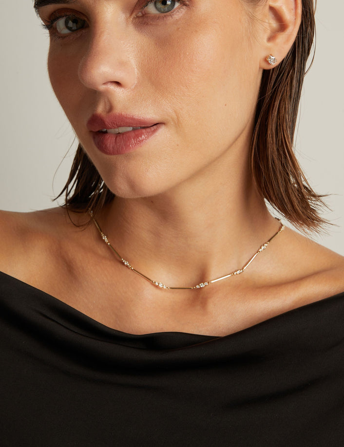 Model. Close up of a woman in a black top wearing a diamond bar necklace on beige background.