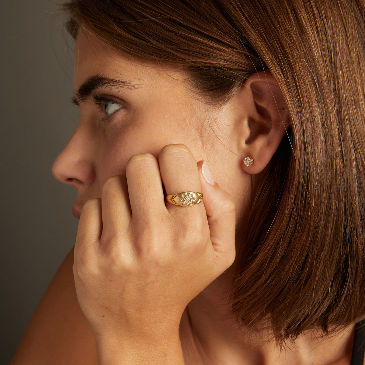 Model. Close up of woman wearing a gold ring with diamonds on neutral background.