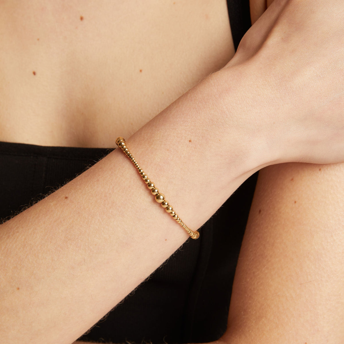 Model. Gold bracelet on a person's wrist with a neutral background.