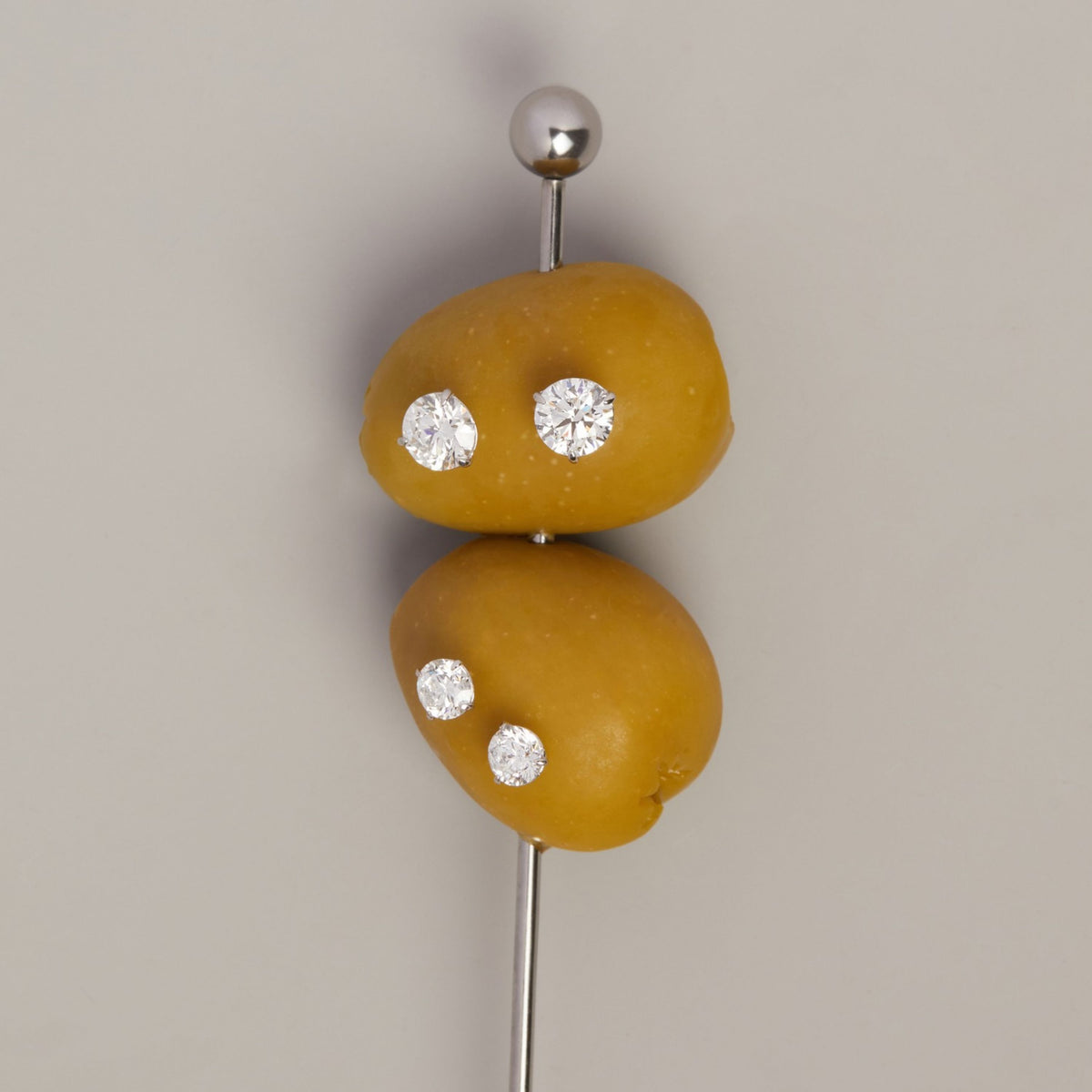 Model. Two pairs of diamond stud earrings on olives on a metal skewer. 