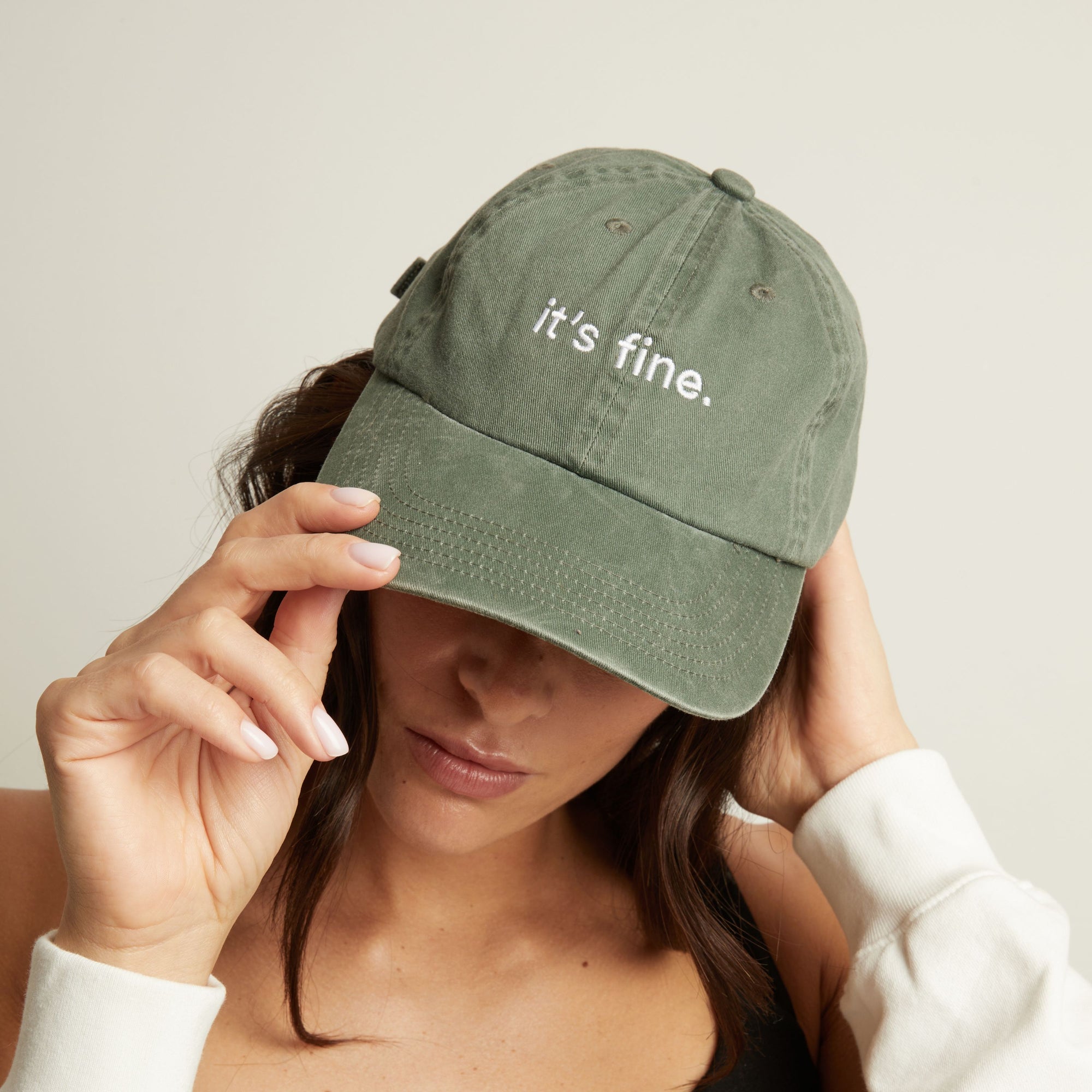 Model. Woman wearing a green cap with 'it's fine' text on a plain background