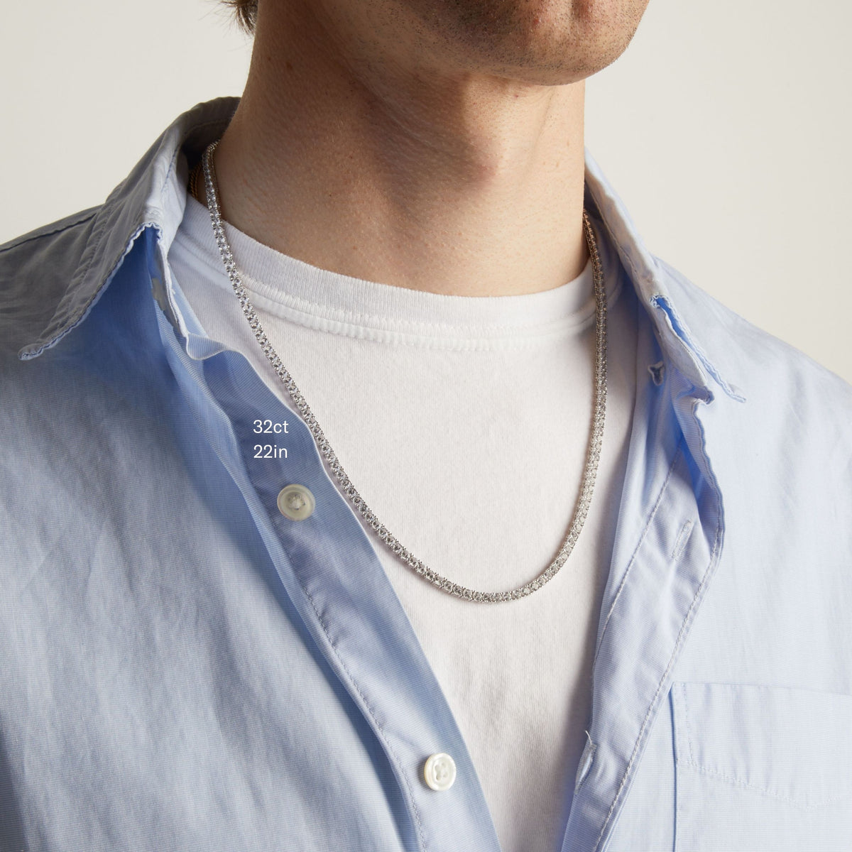 Model. A close-up of a man wearing a tennis necklace over a white t-shirt and a light blue button-down shirt.