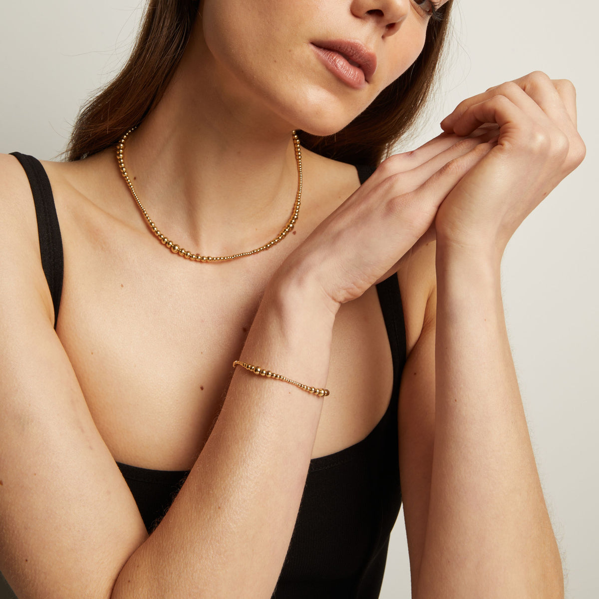 Model. Woman wearing gold necklace and bracelet against a neutral background.