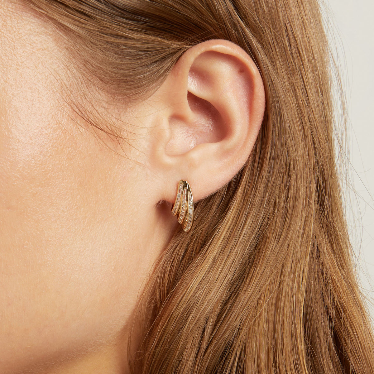 Model. A close-up of a woman wearing a small gold hoop earring with textured, baguette gemstone detailing.