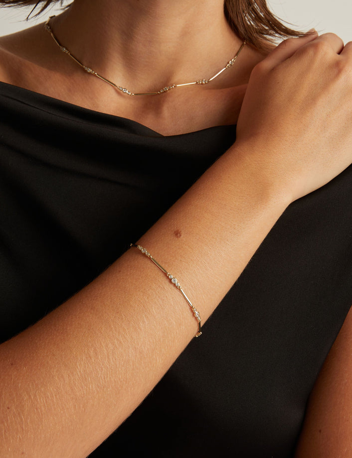 Model. Close up of woman wearing a black shirt with a diamond bar bracelet and necklace on beige background.