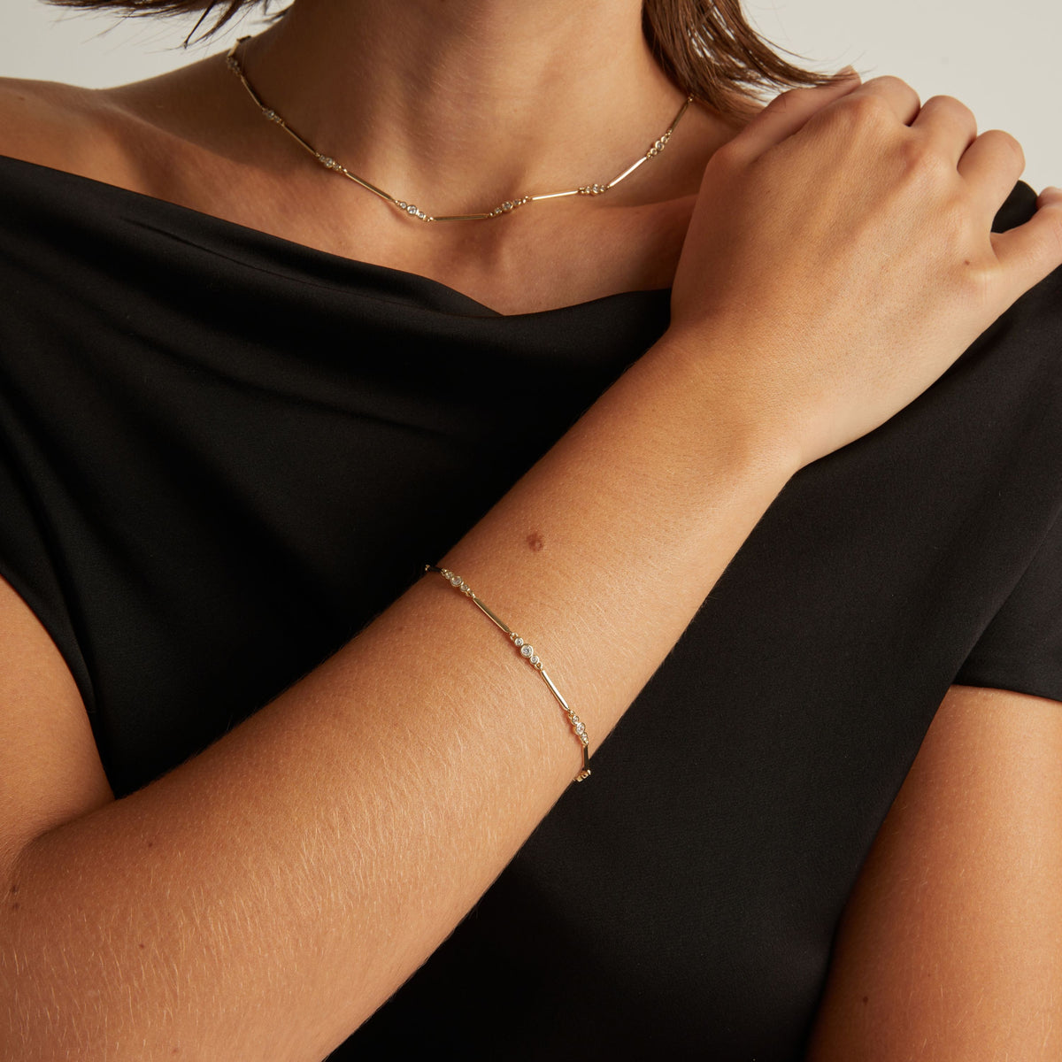 Model. Close up of woman wearing a black shirt with a diamond bar bracelet and necklace on beige background.