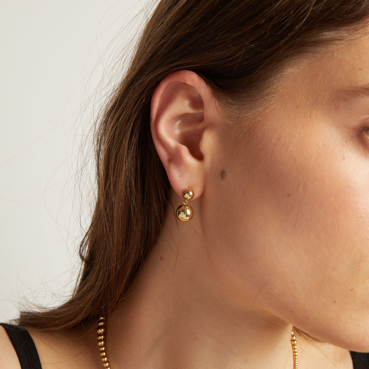 Close up of a person wearing gold earrings with a plain background. 