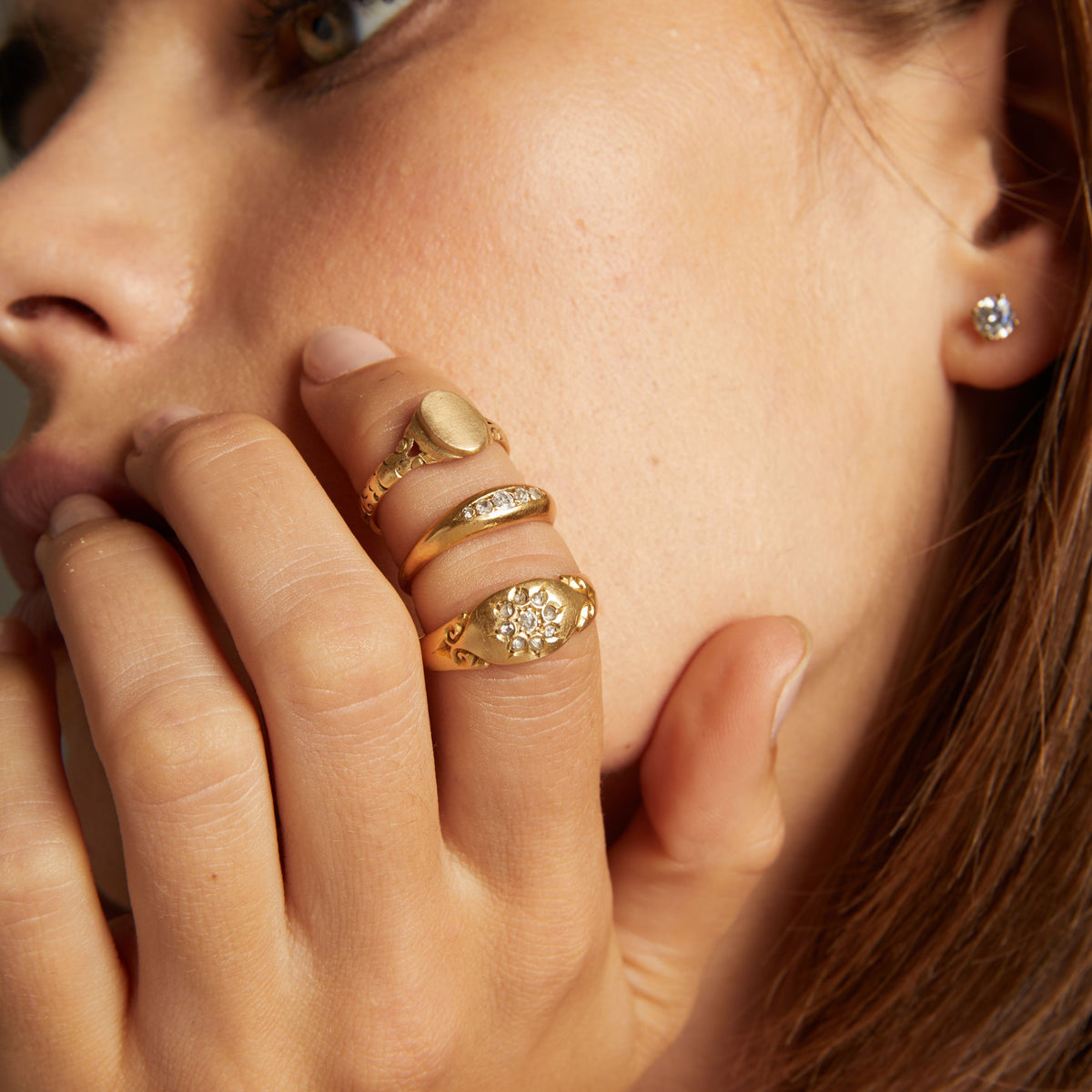 Model. Close up of woman wearing three gold rings on neutral background.