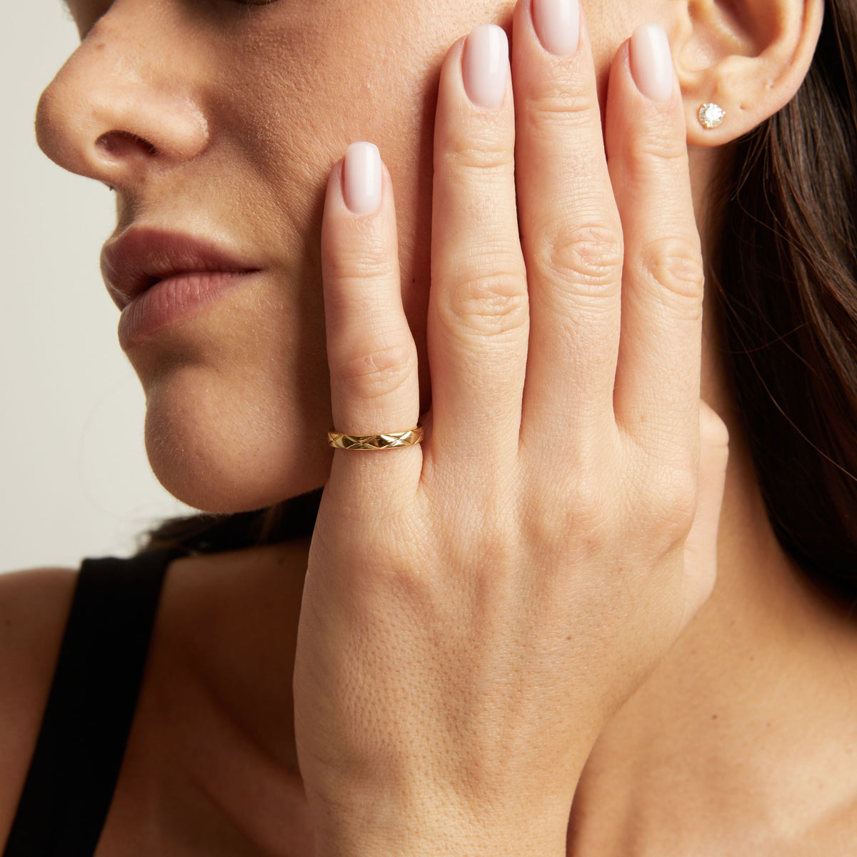 Model. A close-up lifestyle shot of a woman wearing a thin, quilted gold band ring on her finger.