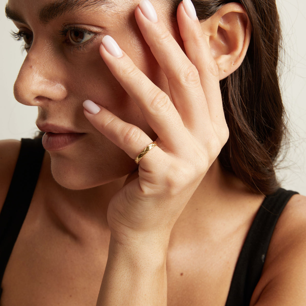Model. A close-up lifestyle shot of a woman wearing a thin, quilted gold band ring on her finger.