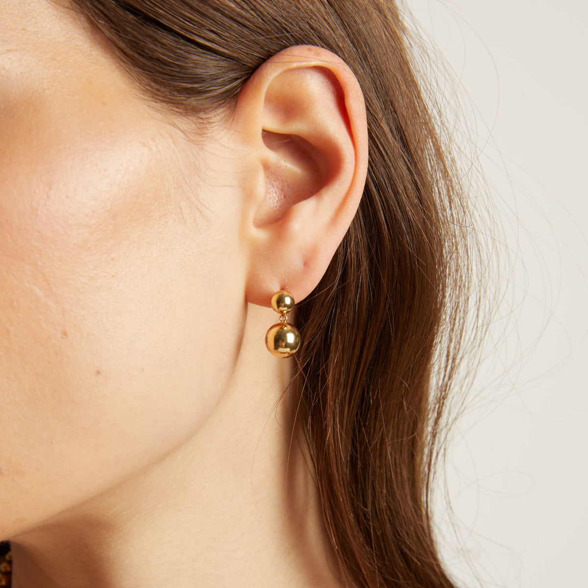 Close up of a person wearing gold earrings with a plain background. 