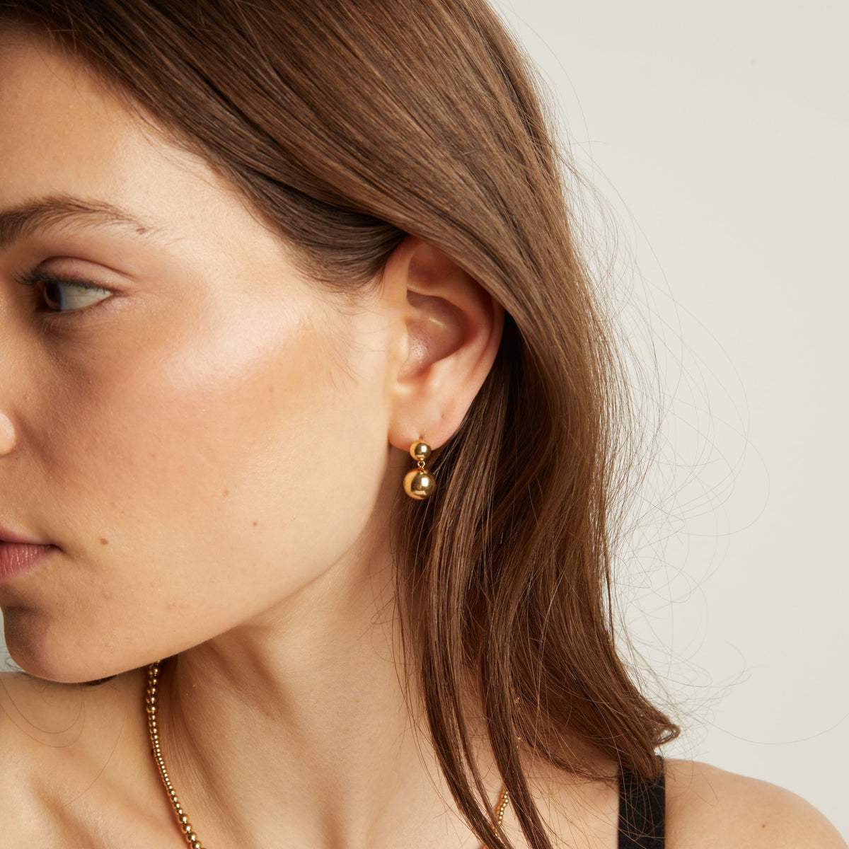 Model. Close up of a person wearing gold earrings with a plain background. 