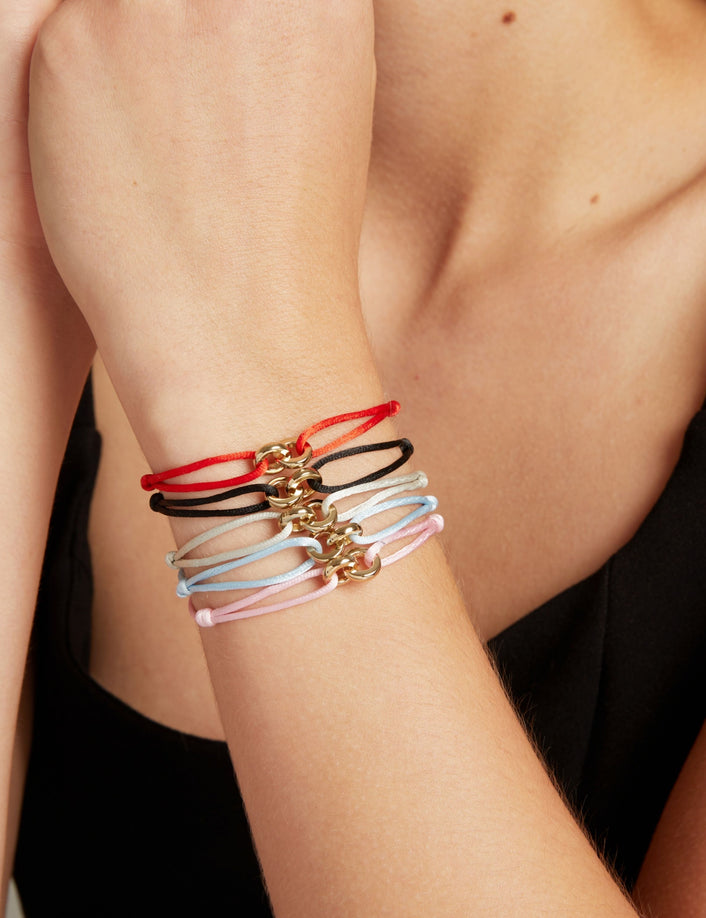 Model. Five delicate cord bracelets, each featuring a small gold-tone clasp, shown stacked on a woman
