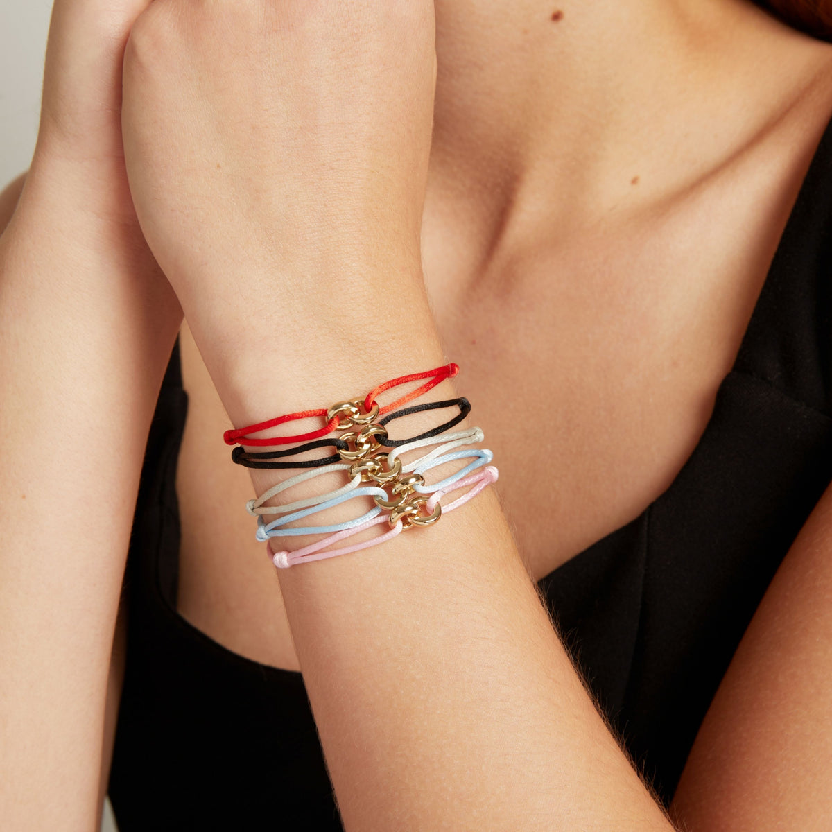Model. Five delicate cord bracelets, each featuring a small gold-tone clasp, shown stacked on a woman's wrist.