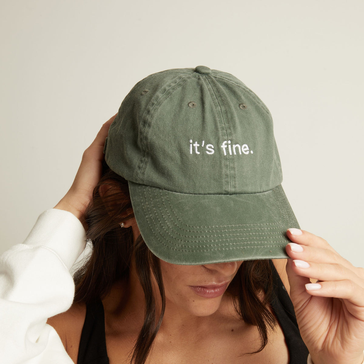 Woman wearing a green cap with 'it's fine' text on a plain background