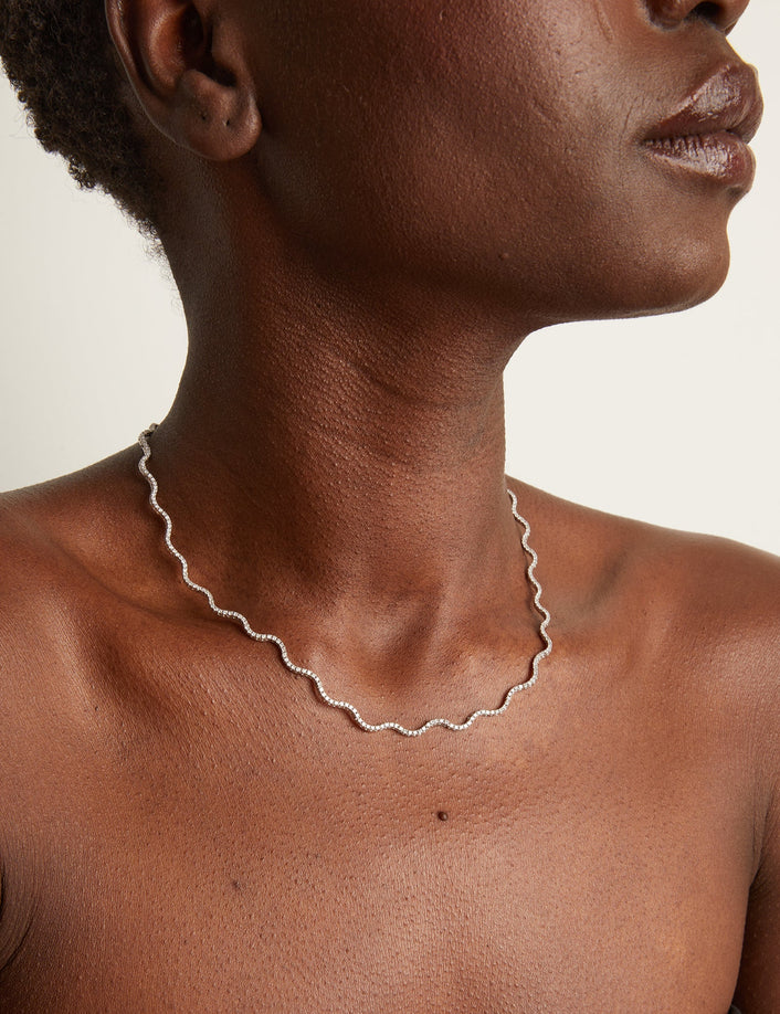 Woman wearing wavy tennis necklace on neutral background
