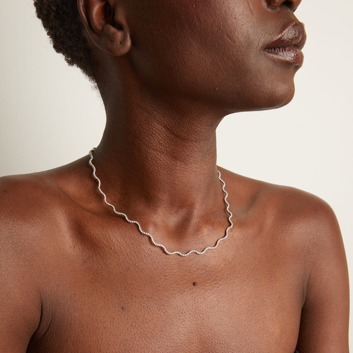 Woman wearing wavy tennis necklace on neutral background