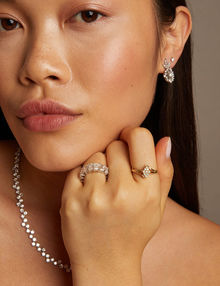 Model. Woman wearing jewelry including earrings, a necklace, and rings against a neutral background