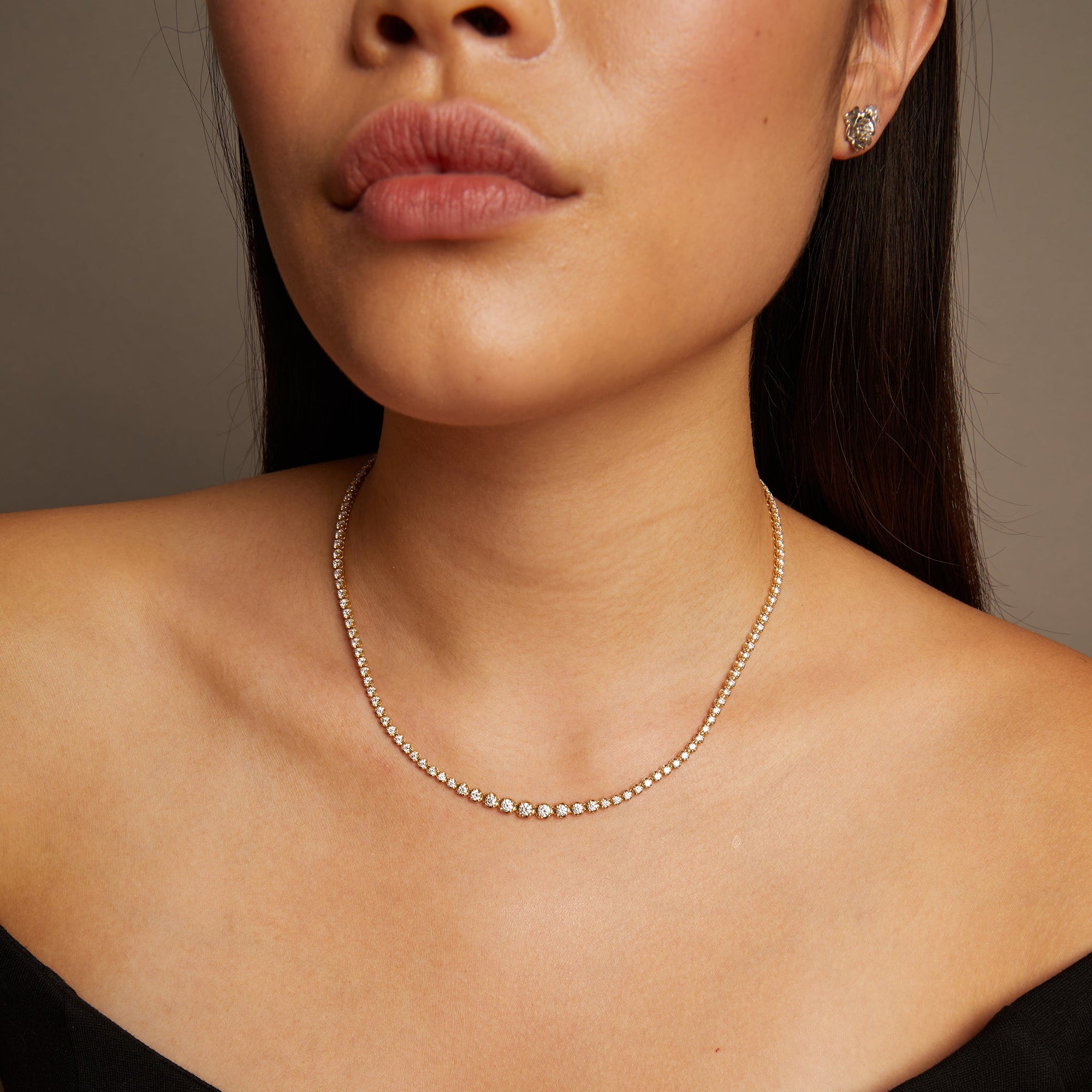 Model. Close-up of a woman wearing a delicate necklace and earrings against a neutral background