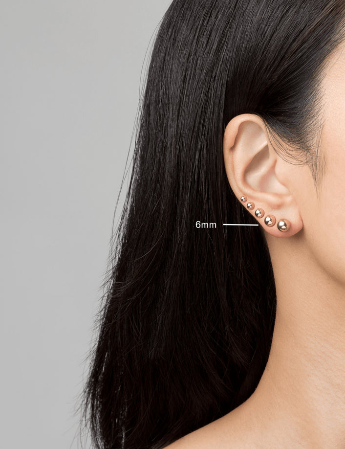 Model. Woman wearing various gold ball earrings on neutral background.