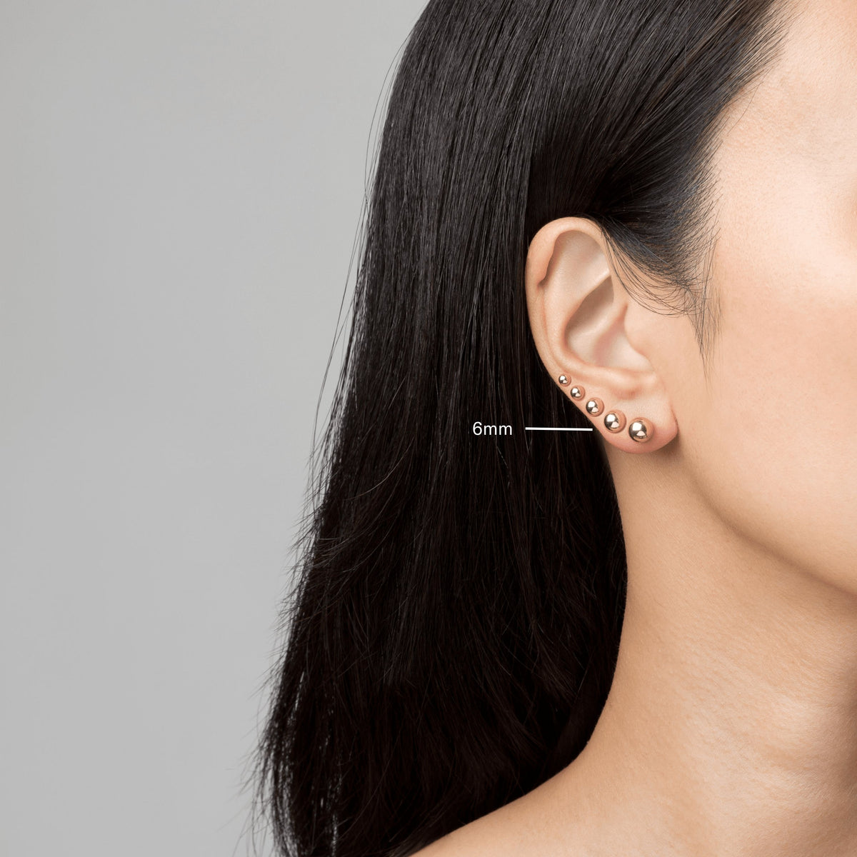 Model. Woman wearing various gold ball earrings on neutral background.