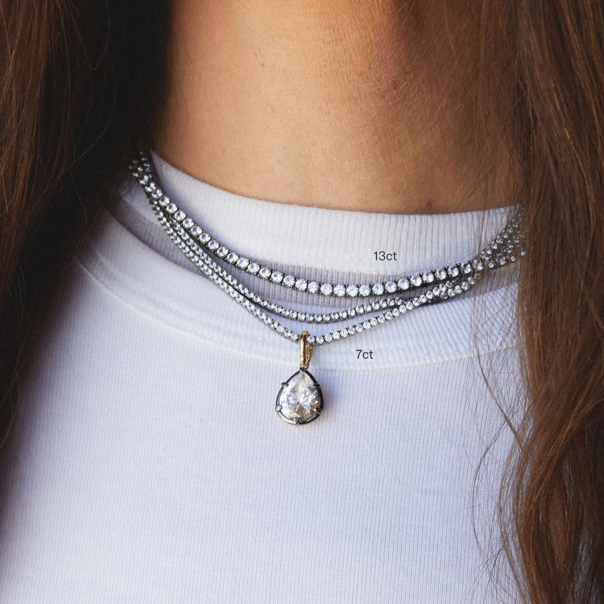 Model. Close up of woman wearing stacked tennis necklaces with pear shaped gemstone pendant. 