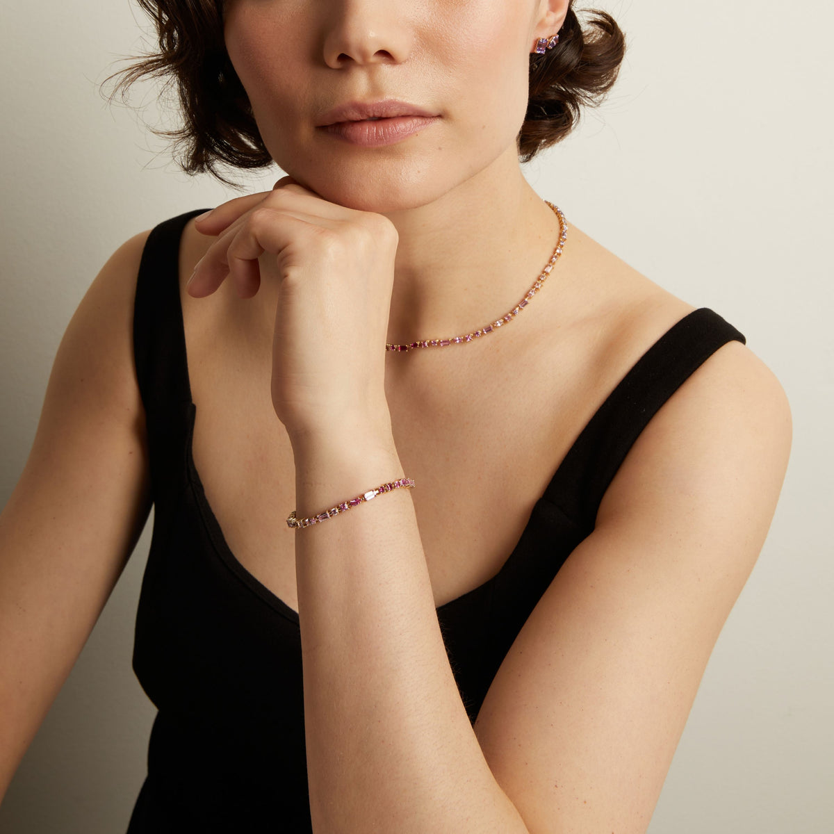 Model. Woman wearing a pink tennis necklace and bracelet with a neutral background